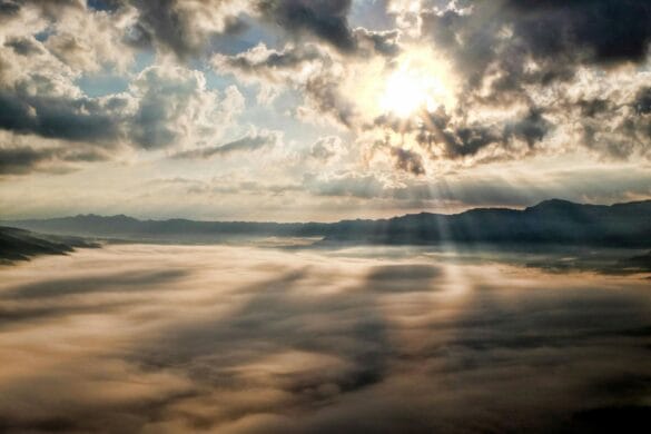 Captivating view of the sun breaking through clouds over a mist-covered mountain range.
